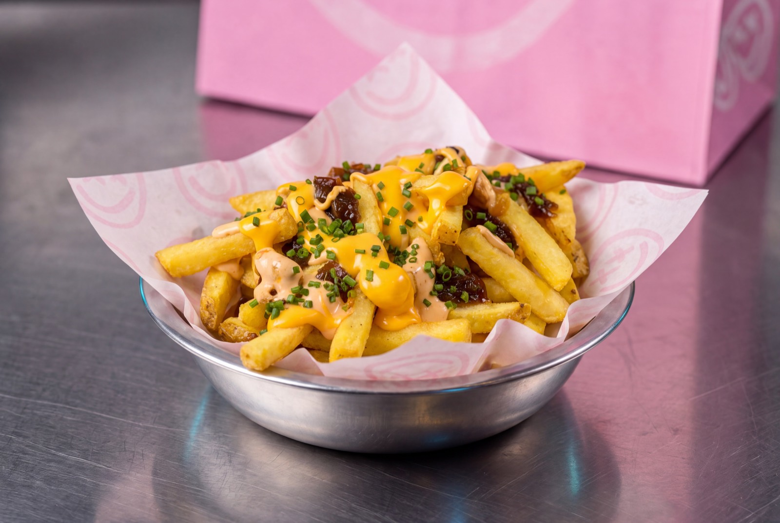 Skin-on fries in a metal bowl loaded with cheese sauce, house sauce, burnt ends and chives.